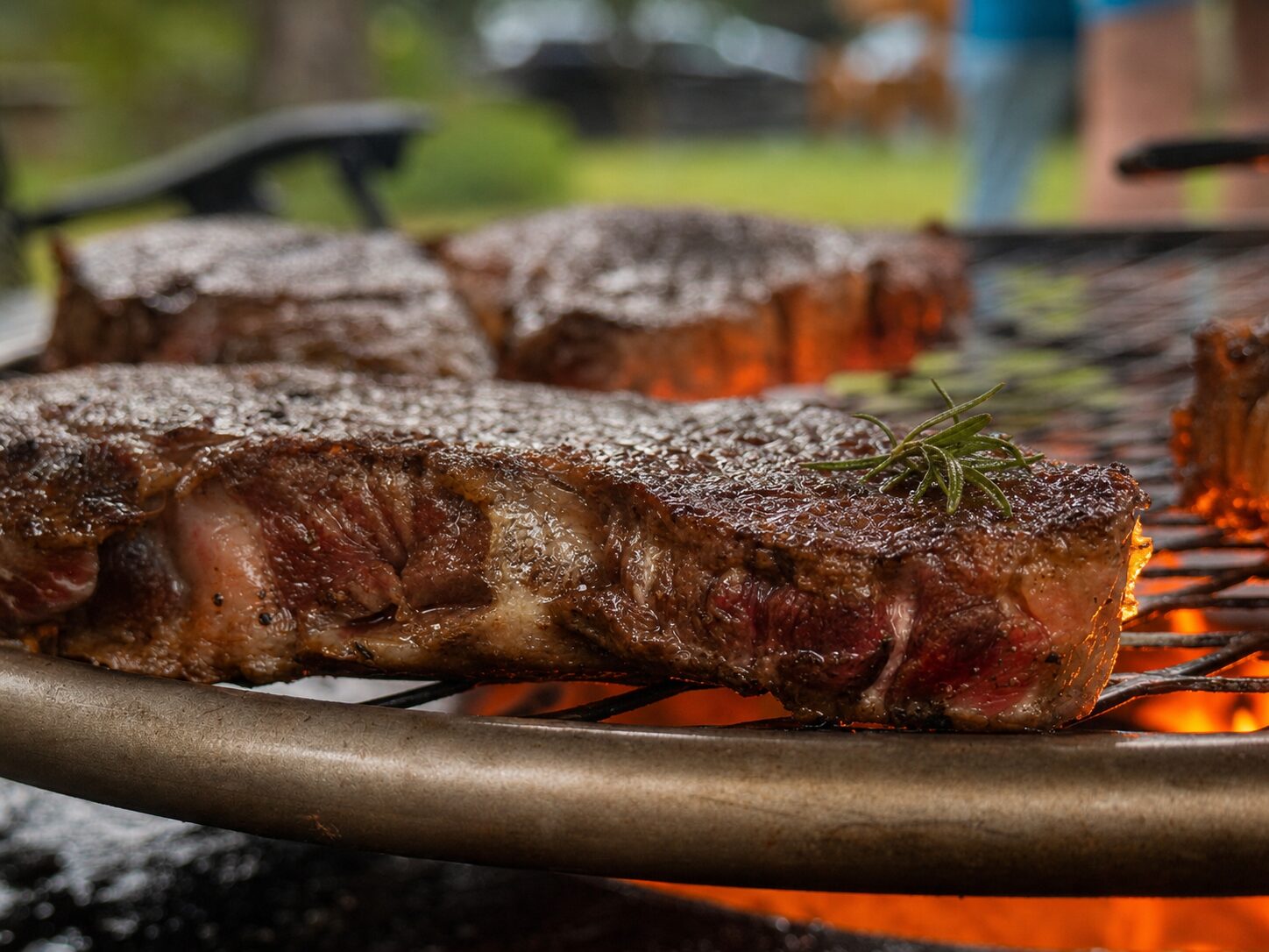 Ribeye steaks searing on a grill grate over open flames